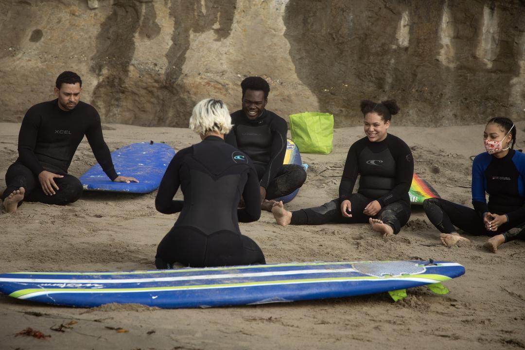 Black surfers gathered in a circle on a beach