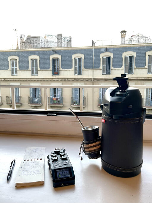 coffee, a voice recorder, and a writing pad with pen on a desk looking out at a building